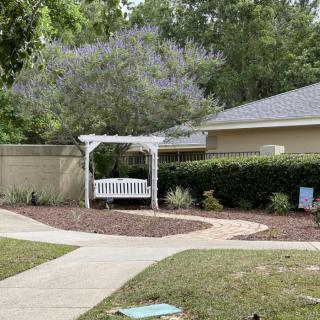 A tranquil garden area with a white pergola and bench, surrounded by greenery and a curved pathway.