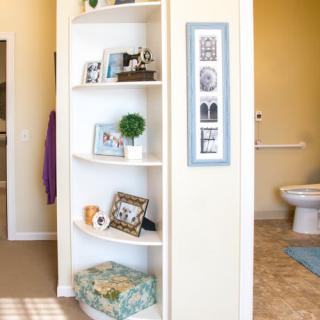 A home interior featuring a white corner shelf with decorative items, adjacent to a bathroom area.