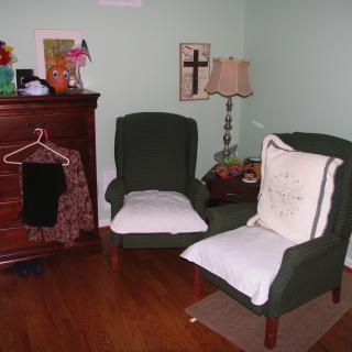 A cozy living room corner with two armchairs, a dresser, and ambient lighting.