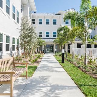 A modern residential building with a landscaped pathway and palm trees under a clear sky.