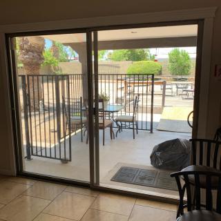 View from inside through a sliding glass door showing a patio with outdoor furniture and a metal fence.