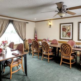 A neatly arranged meeting or dining room with wooden tables and chairs, decorated with curtains and wall art, featuring a ceiling fan and an American flag in the corner.