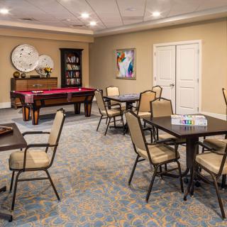 A well-lit recreation room featuring a pool table, multiple tables with chairs, and decorative artwork on the walls.