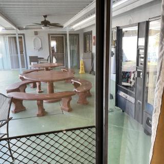 A covered patio area with a large table and benches, featuring green flooring and a ceiling fan.