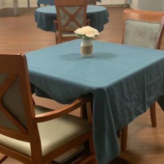 A dining table with a blue tablecloth and a flower vase in an interior setting.