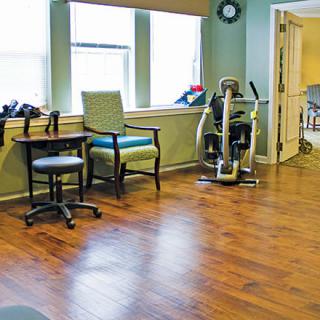 A brightly lit room with exercise equipment and chairs, featuring a hardwood floor.