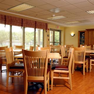 A bright dining room with wooden tables and chairs, featuring large windows that allow natural light to flood the space.
