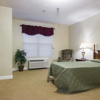 A neatly arranged hotel room with a single bed, a lamp on the bedside table, an upholstered chair, and a window with curtains.