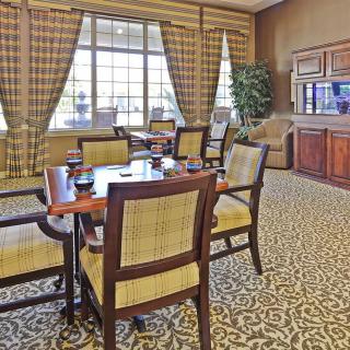 A well-furnished meeting room with a central table, chairs, and large windows with plaid curtains.