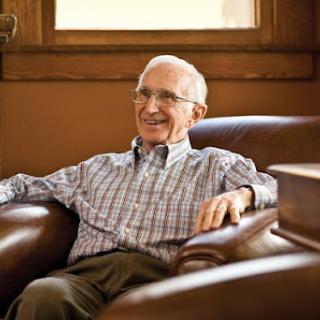 An elderly man sitting comfortably in an armchair, smiling warmly.