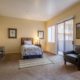 A cozy bedroom featuring a single bed, minimalist decor, and a flood of natural light from large windows.