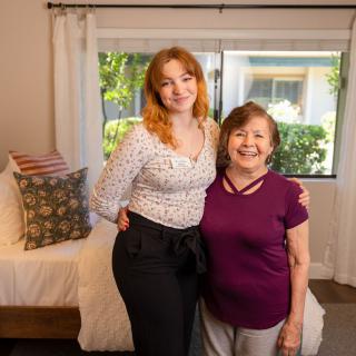 Two people smiling inside a bedroom.