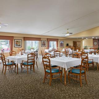 A spacious dining room with neatly arranged tables and chairs, featuring large windows and warm decor.