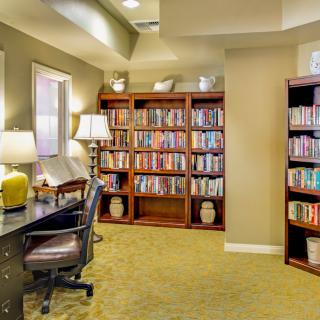 A cozy library corner with bookshelves, a desk, and a reading lamp.