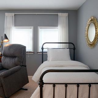 A cozy bedroom with a single bed, recliner chair, and decorative mirror on the wall.