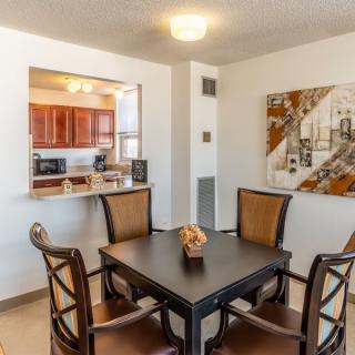 A modern dining area with a table and four chairs, featuring a view into the kitchen.