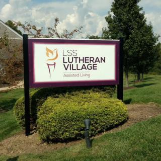 A sign for LSS Lutheran Village Assisted Living surrounded by greenery.