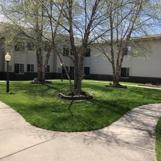 A neatly landscaped outdoor area featuring a building surrounded by trees, grass, and pathways.