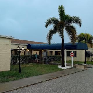 A view of a building entrance with palm trees under a cloudy sky.