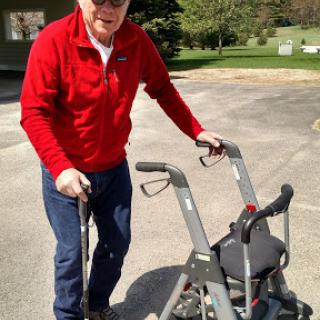 An elderly man using a walker in an outdoor setting, dressed in a red jacket.