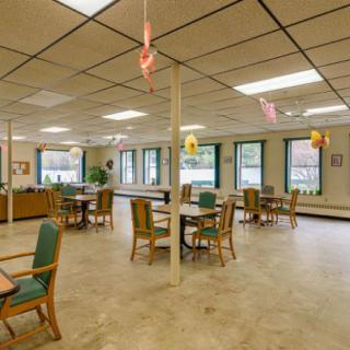 A spacious dining area with tables and chairs, featuring large windows and overhead lighting.