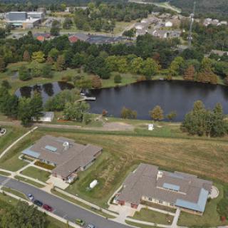 A serene aerial view of a suburban residential area near a pond, surrounded by lush greenery.