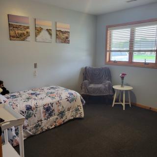 A cozy bedroom with a single bed, artwork on the wall, and a window letting in natural light.