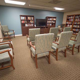 A cozy library room with arranged chairs facing a television and bookshelves filled with books.
