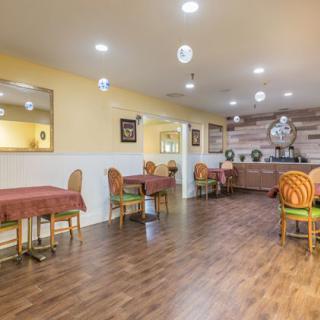 A cozy dining area with neatly arranged tables and chairs, featuring warm lighting and wooden flooring.