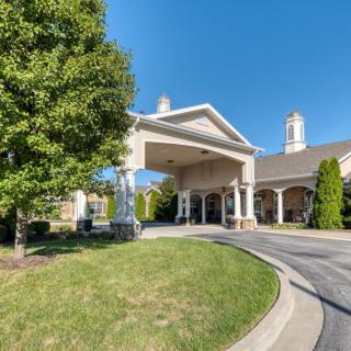 A large building entrance with a covered driveway and surrounding greenery on a sunny day.