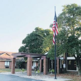A building entrance with a flagpole displaying the American flag, surrounded by trees.