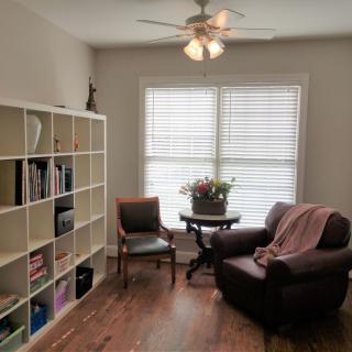 A cozy living room with a bookshelf, armchair, and large window.