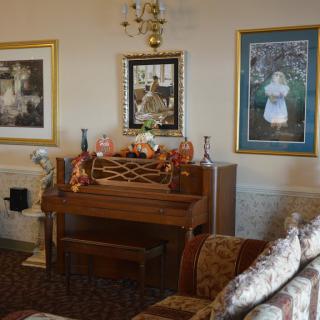 A cozy living room featuring a classic piano, adorned with decorative items and surrounded by artwork.