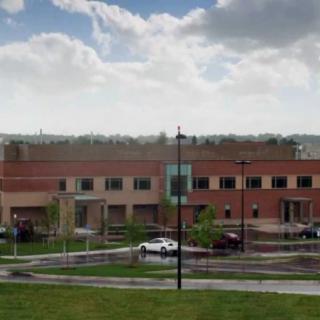 A brick building with a parking lot and cars in front, set against a cloudy sky.