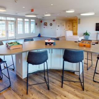 A modern kitchen with a curved counter and bar stools, featuring bright lighting and wood flooring.