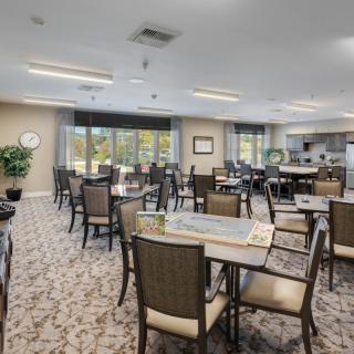 A spacious and well-lit dining area with multiple tables and chairs, surrounded by large windows and decorative plants.