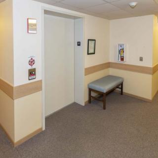 A hallway with an elevator and a bench on the side.