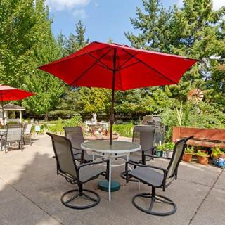A peaceful outdoor patio area with a table, chairs, and a red umbrella, set in a lush garden setting.