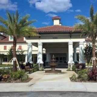 A beautiful building entrance with palm trees and a fountain under a sunny sky.