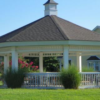A charming gazebo surrounded by greenery in a sunny park setting.