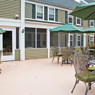 An outdoor patio area with tables, chairs, and green umbrellas in front of a building.