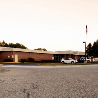 A view of a school building with parked vehicles and an American flag flying at sunset.