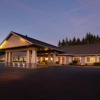 A well-lit building exterior during the evening with a parking lot in front and trees in the background.