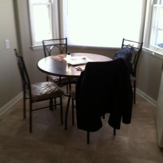 A small dining area with a round table and chairs, illuminated by natural light from the windows.