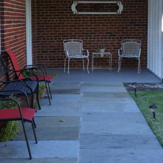 A porch with multiple chairs and a small table set against a brick wall.
