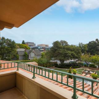 A scenic view from a balcony overlooking a neighborhood with lush trees and houses under a clear blue sky.