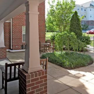 A sunny outdoor patio with garden furniture and lush greenery beside a brick building.