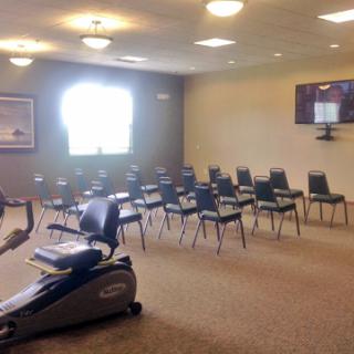 A spacious waiting room with chairs arranged neatly and exercise equipment in the corner.