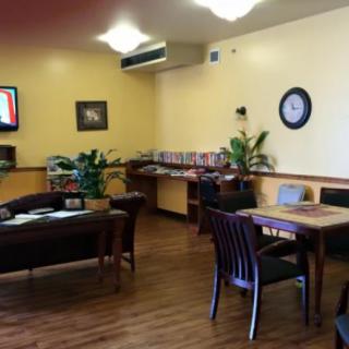 A cozy waiting room with comfortable seating, a table, plants, and reading materials.