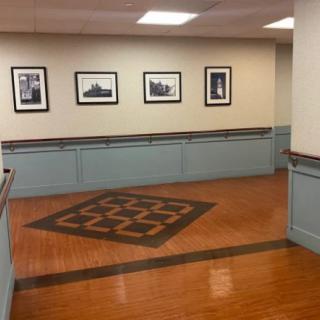 A hallway with wooden flooring, featuring framed photographs on the wall and subtle overhead lighting.